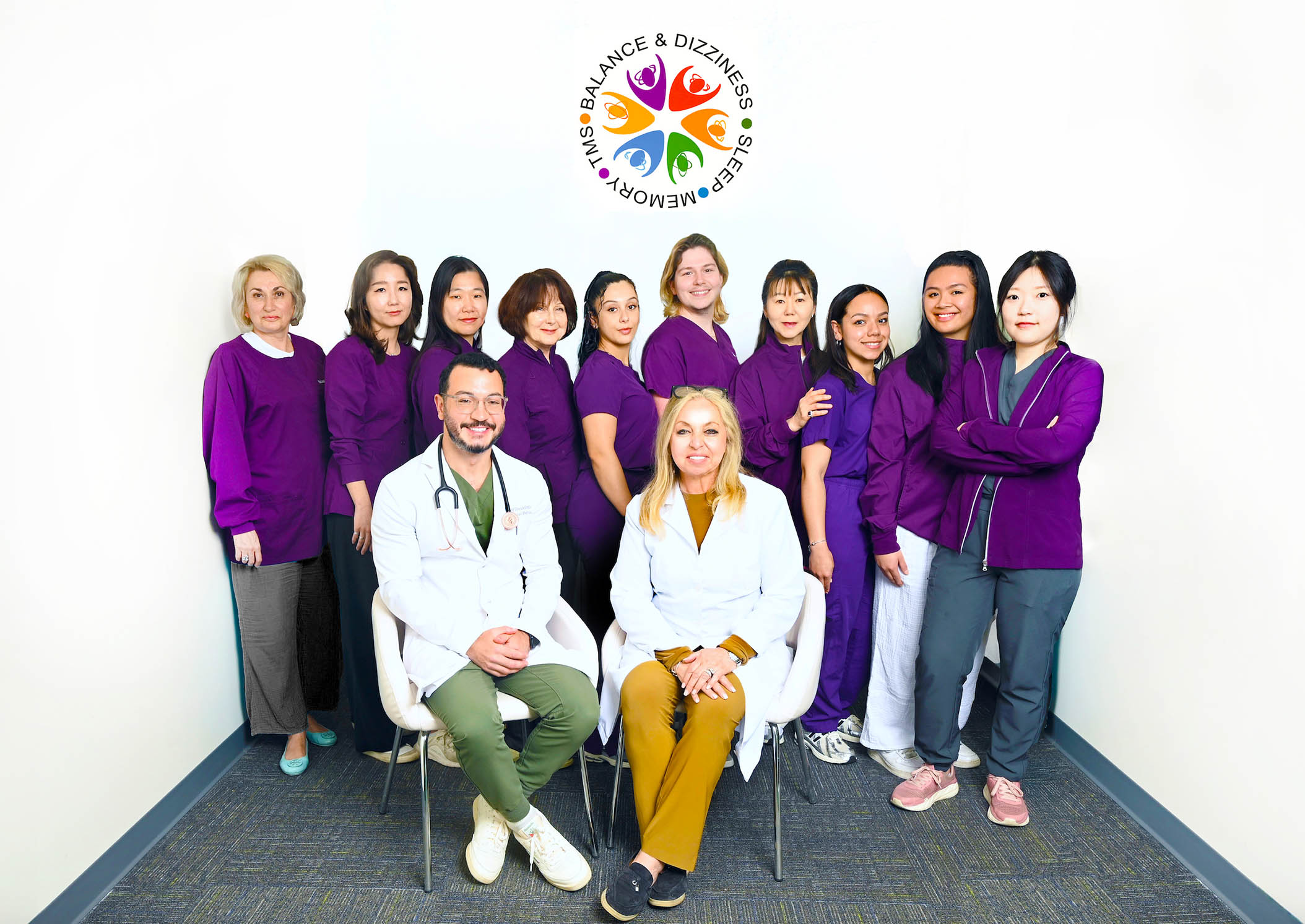 The image shows a group of individuals posing together for a photo, with some people standing and others seated, in front of a backdrop featuring text and logos.