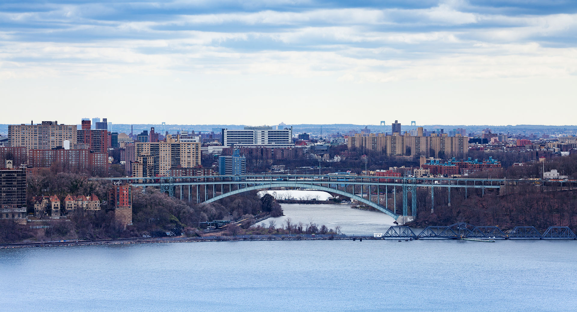 The image shows a cityscape with a large bridge crossing over a body of water, featuring a clear sky and a calm river.