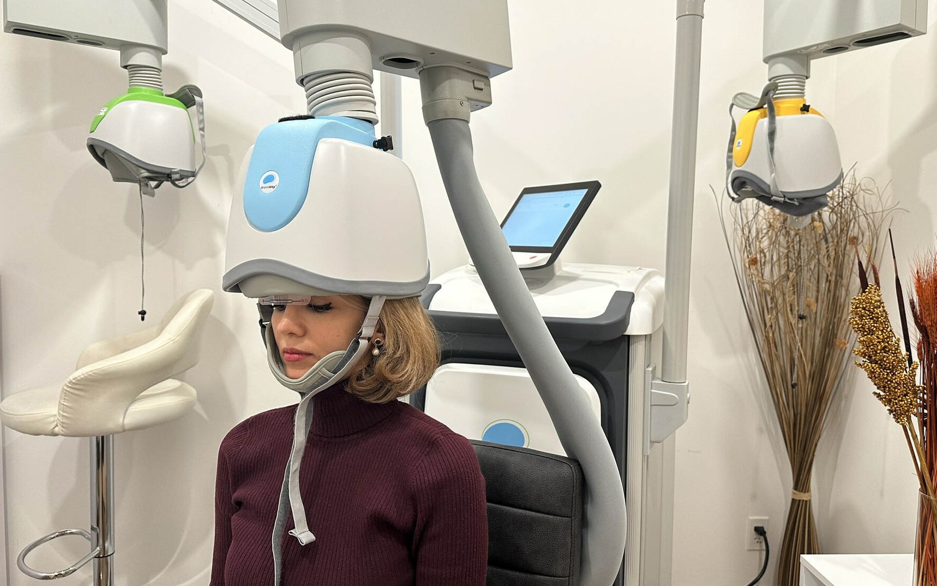 A woman sitting inside a dental chair with a device on her head, likely for dental treatment, set against a backdrop featuring various dental equipment.