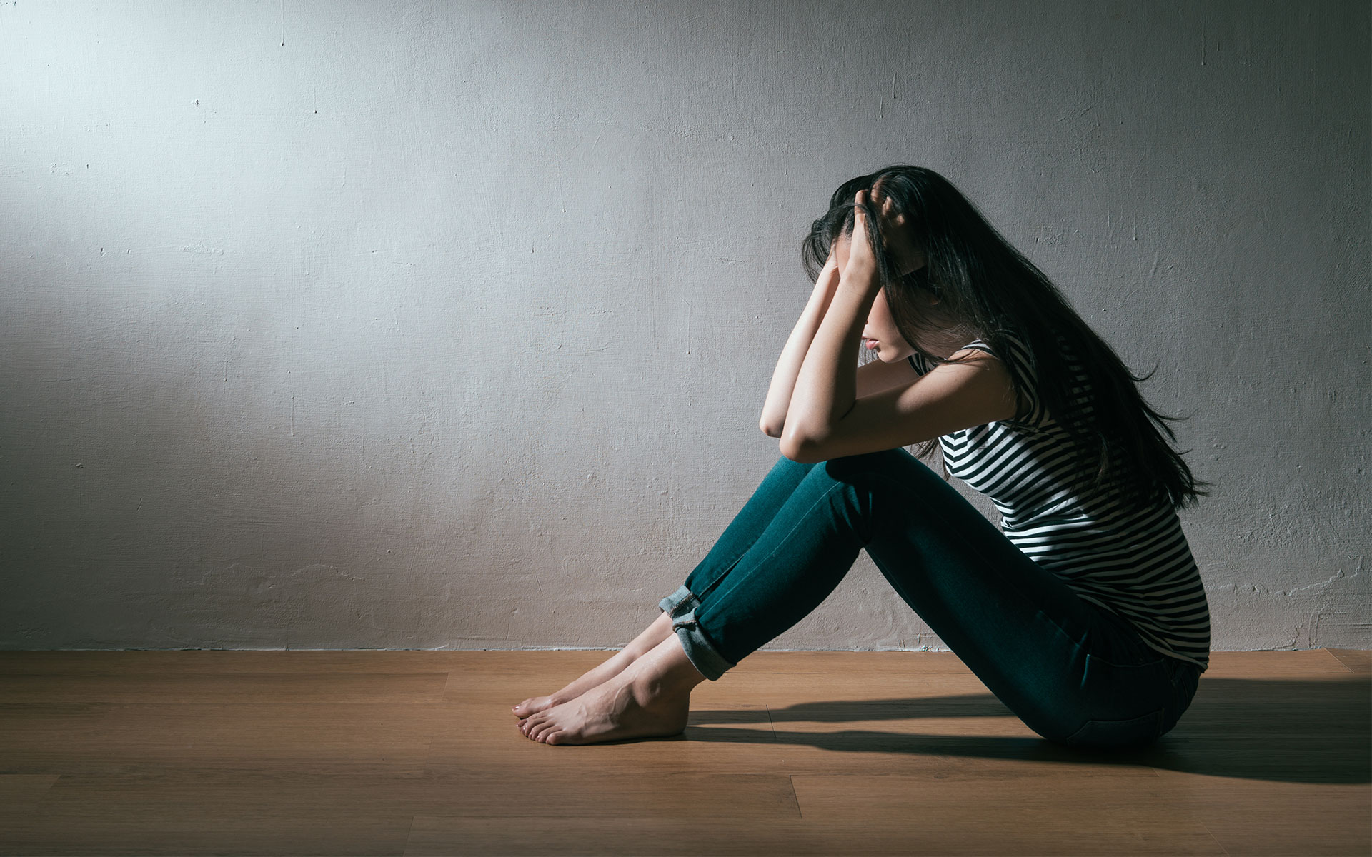 A woman sits on a floor with her head in her hands, appearing distressed.