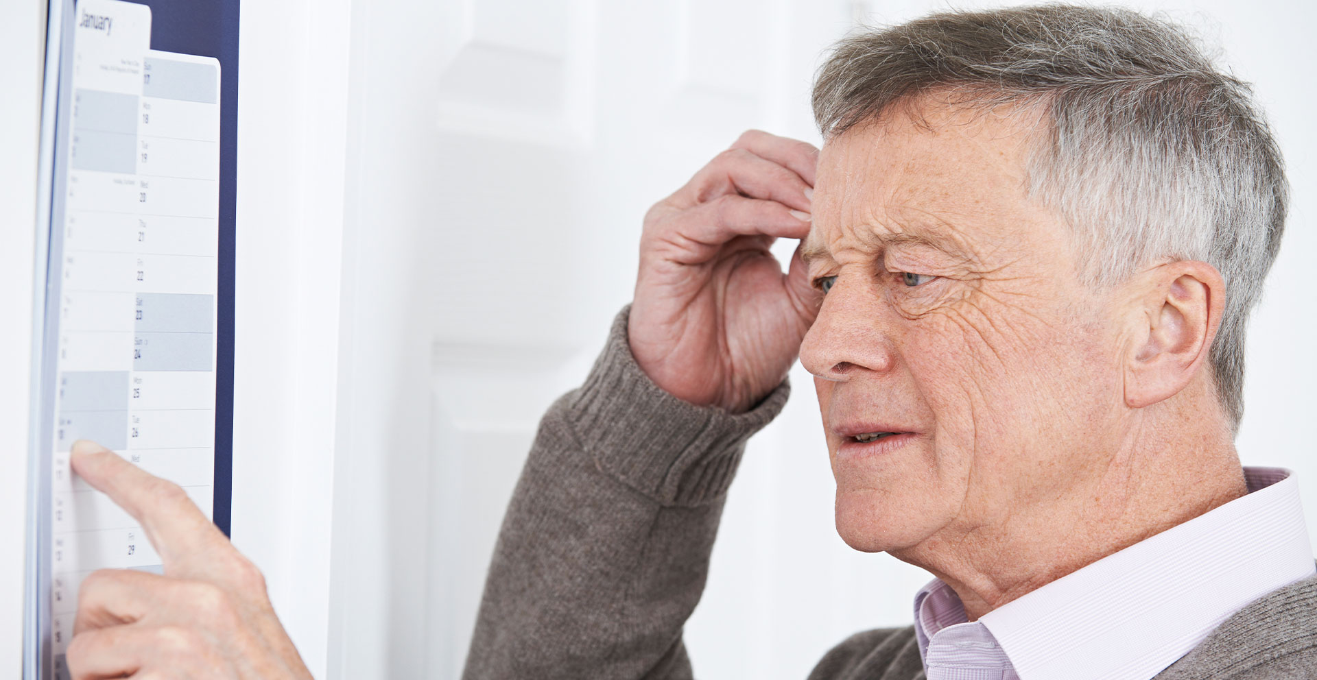 The image shows an older man with his hand on his forehead, appearing to be confused or puzzled, while looking at a calendar with a finger pointing towards a specific date.