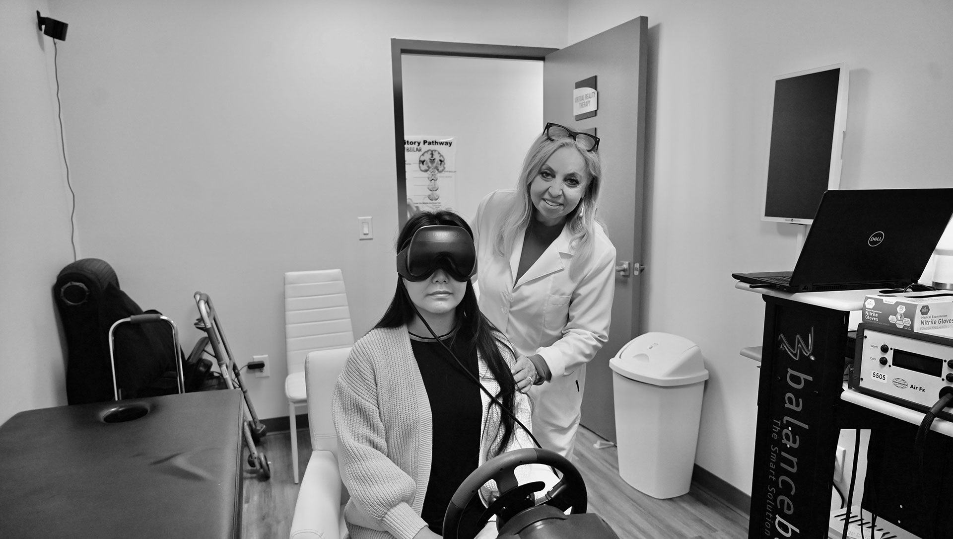 A woman wearing a white coat stands beside a person sitting in a dentist s chair with a virtual reality headset on, inside a dental office.