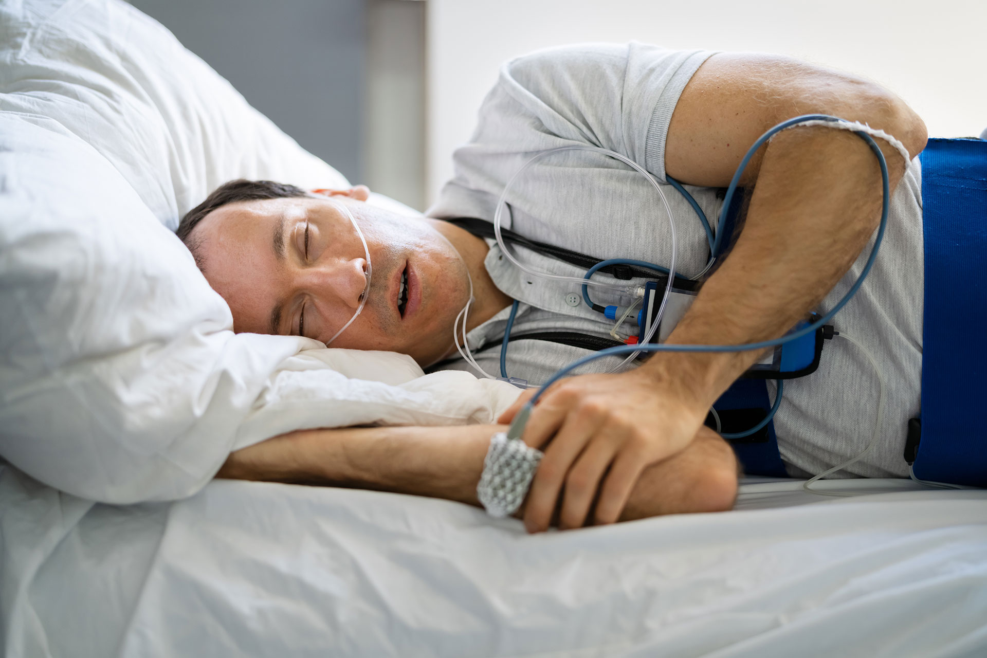 The image shows a man lying in bed with medical equipment attached to him, including an oxygen mask and a heart rate monitor.
