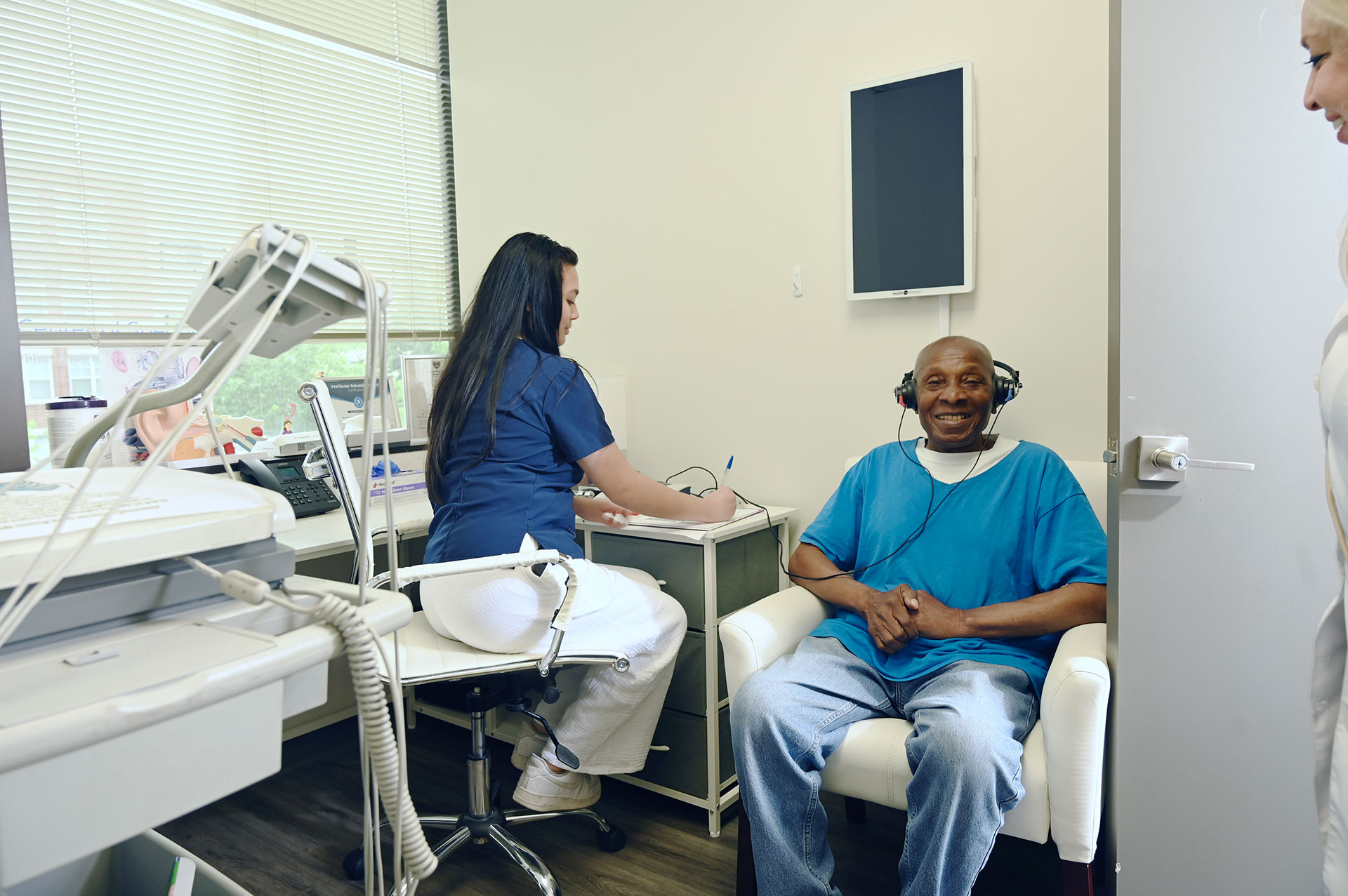 The image shows a man sitting in a dental chair with a dental professional standing next to him, both located within a dental office setting.
